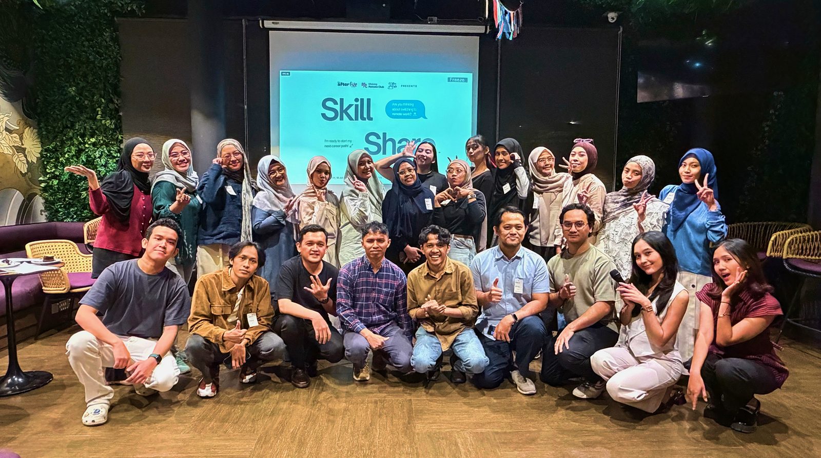 Members of Indonesia Remote Club posing together in front of a “Skill Share” presentation screen at an indoor meetup