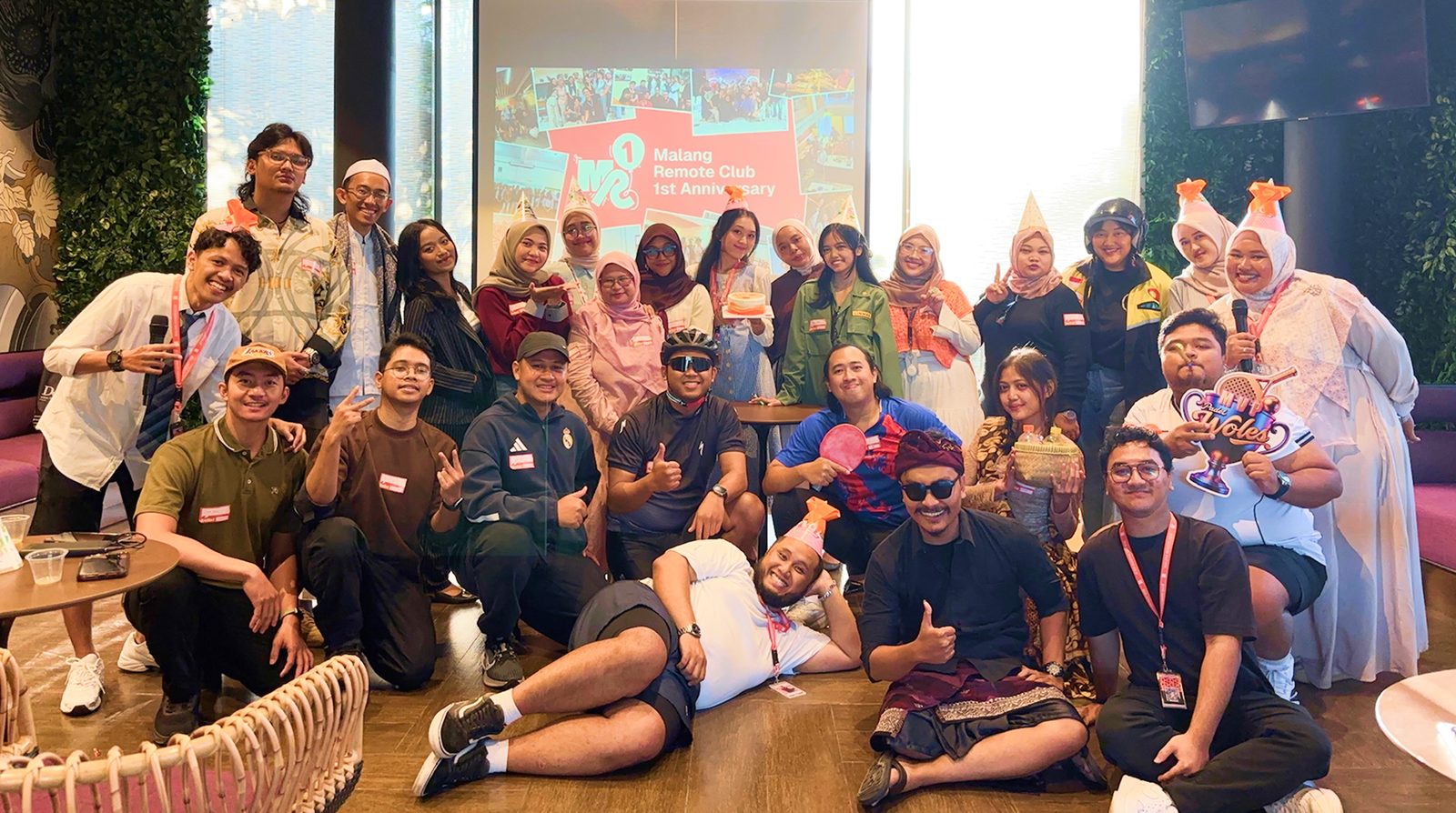 Members celebrating the Malang Remote Club 1st Anniversary, with the event slide projected behind them